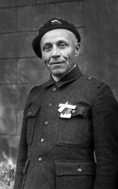 Josef Beran in 1945, a middle aged man in a dark beret and a heavy dark coat with a ribbon and badge pinned to the chest, photographed against a stone wall