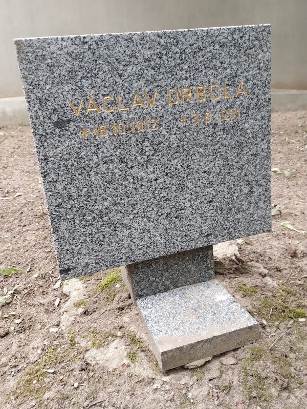 A small granite marker set in bare earth at the Dablice cemetery in Prague, cut in gold letters with the name Vaclav Drbola and the dates 16 October 1912 and 3 August 1951