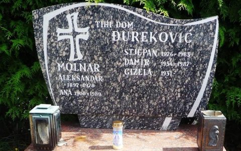 A polished granite headstone carved with a cross and the words TIHI DOM ĐUREKOVIĆ, listing Stjepan 1926 to 1983, Damir 1954 to 1987 and Gizela 1931, with the Molnar family names on the left and lanterns and a candle at its foot