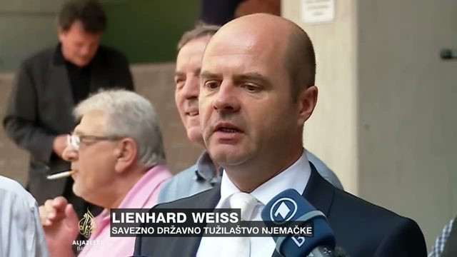 A man in a dark suit and white tie speaking into a microphone outside a court building, captioned Lienhard Weiss of the German federal prosecutor's office, with other people standing behind him