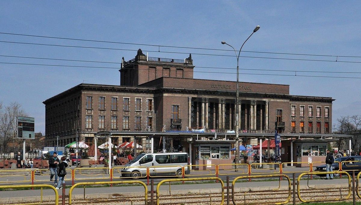 The Palace of Culture in Dabrowa Gornicza, a long brick building with a columned portico, seen across the tram tracks