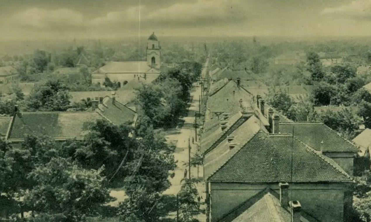 A period postcard view over the roofs of Tiszafoldvar, a church tower and a long unpaved street