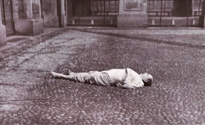 The paved courtyard of the Czernin Palace with the arcade behind: a man in pyjamas lying on his back on the cobbles, barefoot, his head turned to one side
