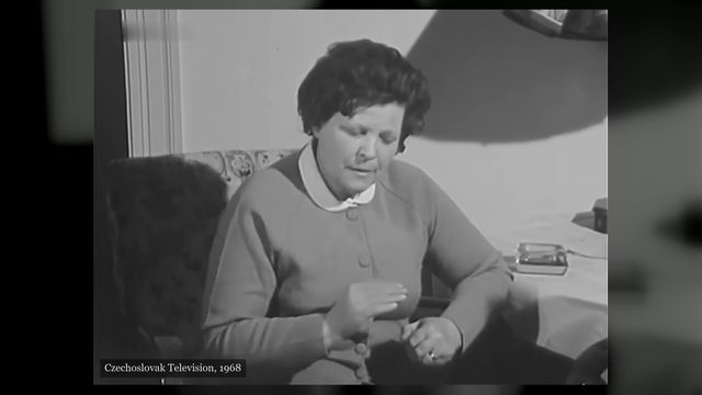 Marie Topinková seated on a sofa in a flat, in a buttoned cardigan and a white collar, her hands raised in front of her as she speaks, filmed by Czechoslovak Television in 1968