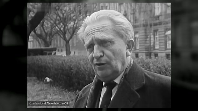 Jaromír Tesař, white haired, in a dark coat and tie, standing in a city park with bare trees and a large building behind him, filmed by Czechoslovak Television in 1968