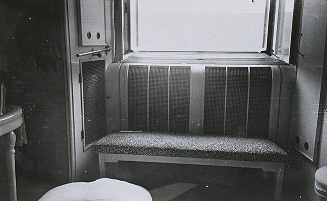 The bathroom window of Jan Masaryk's flat from inside on 10 March 1948: the window opening with a grille across its lower half, a fixed bench with a padded top beneath it, a pillow on the floor to the left and the pedestal of a washbasin beyond