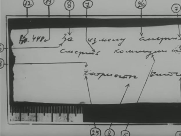 A torn slip of paper photographed against a ruler, carrying three short lines of Cyrillic handwriting, with numbered pointers drawn to individual letters