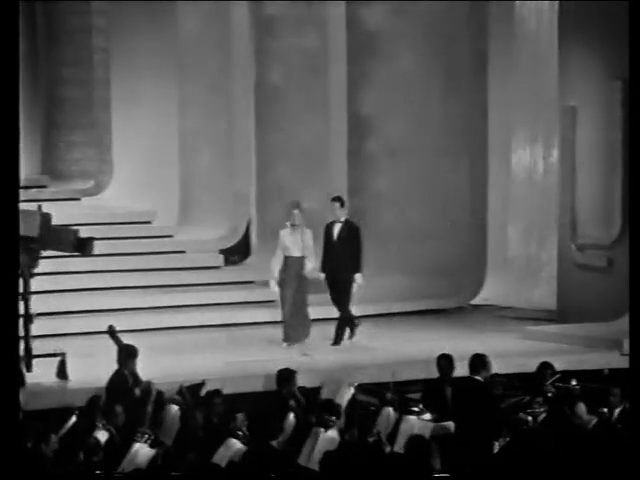 The Golden Stag stage in Brasov in March 1971: two presenters walk across a wide stage under tall curved set pieces, with the orchestra and the audience in the foreground