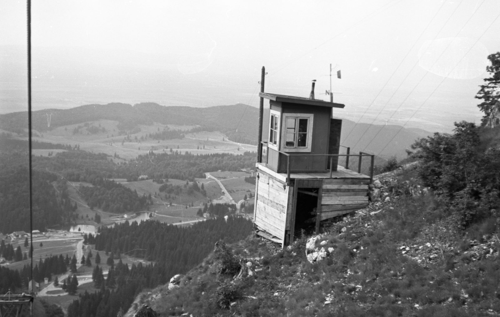 The Poiana Brașov basin seen from the mountain above it in 1969: a wooden cable lift station standing on the slope in the foreground, and below it the resort, its lake and its spruce woods in the valley