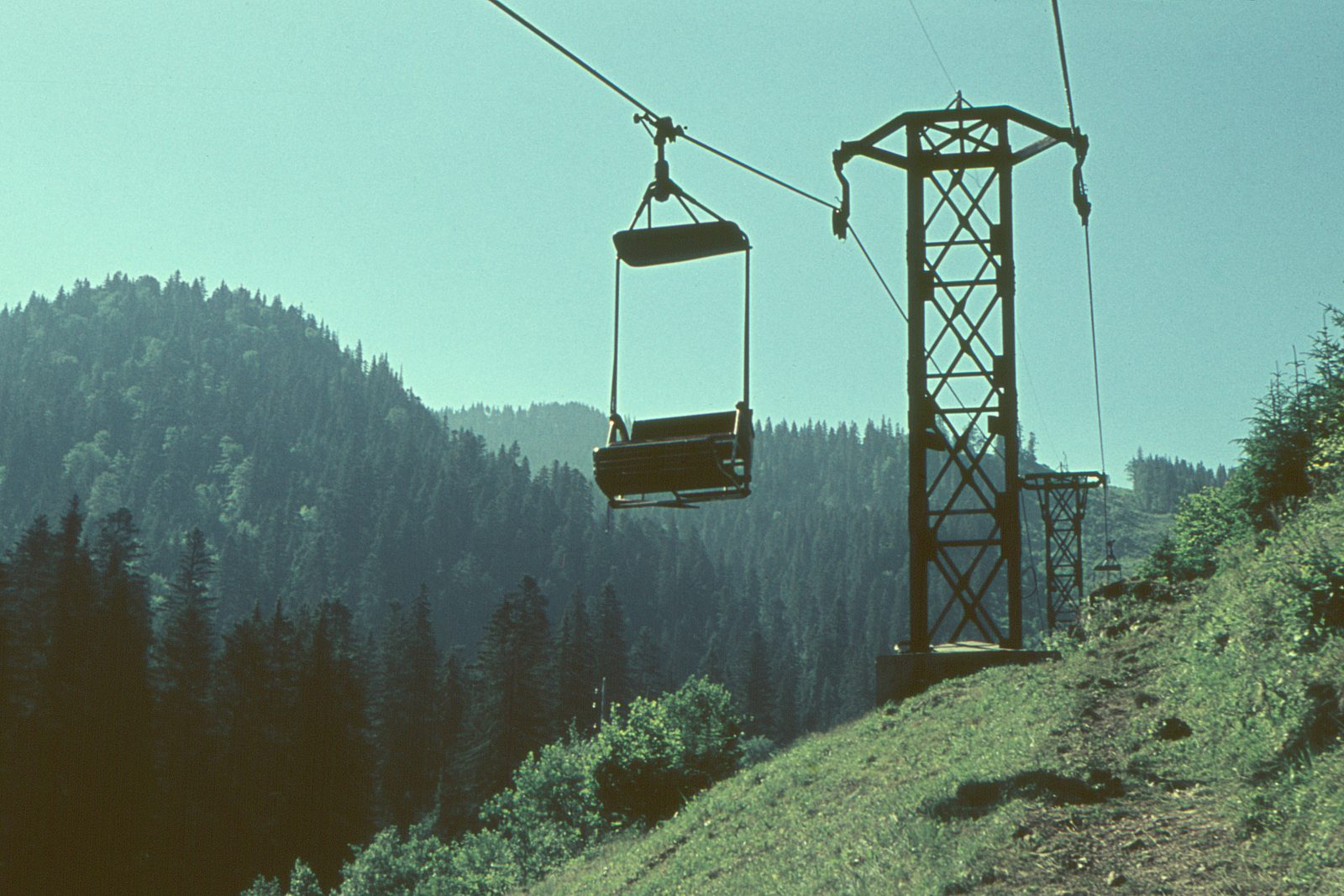 A double seat chairlift running up the wooded slope to the Postăvarul mountain above Poiana Brașov, photographed on 5 July 1964