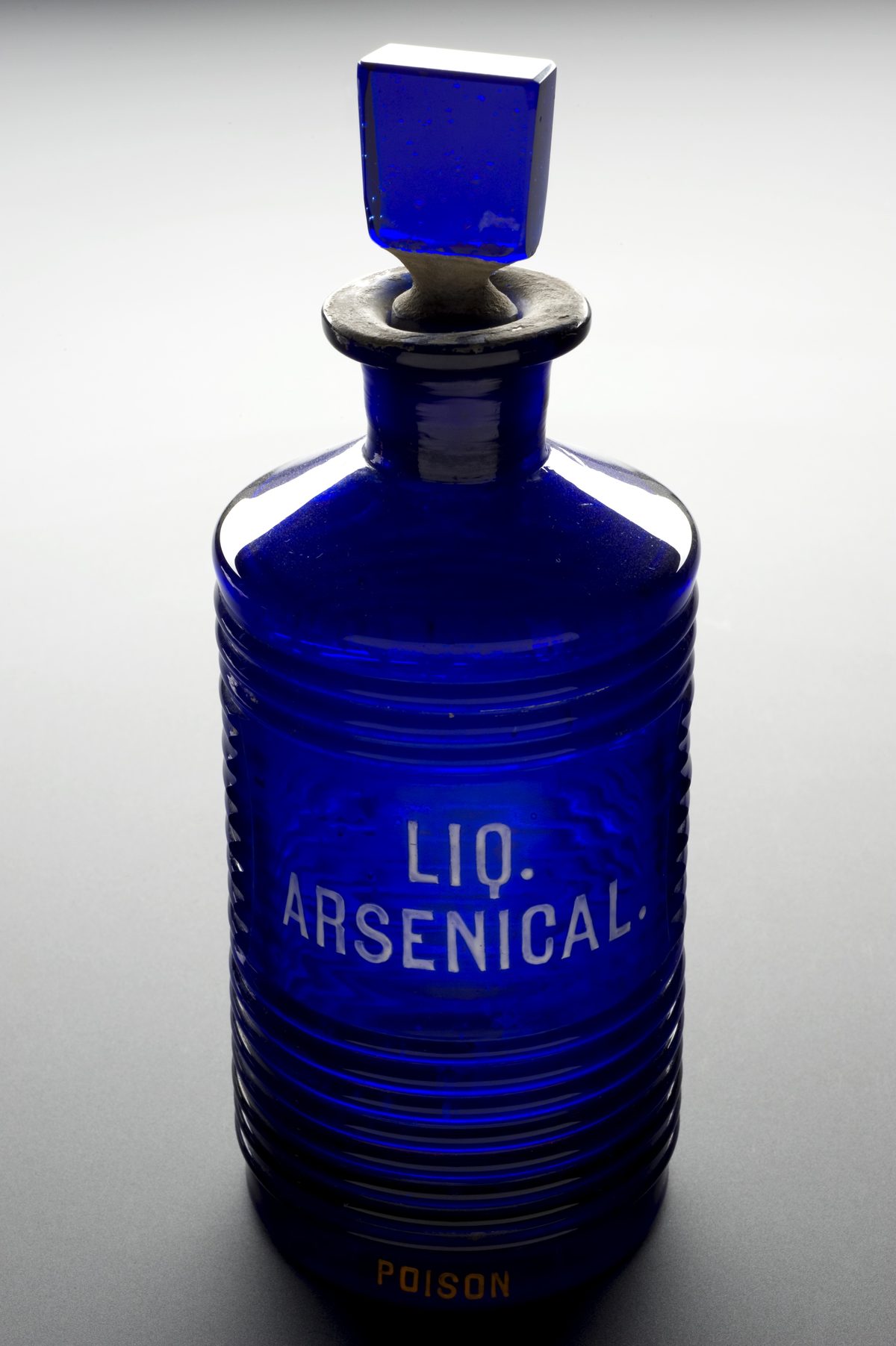 A blue ridged glass bottle used for arsenic in Europe between 1701 and 1935, photographed against a plain ground