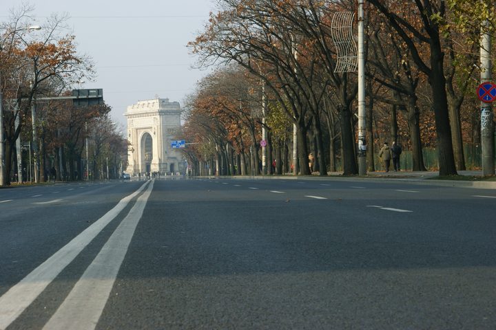 The Arch of Triumph in Bucharest seen down an empty tree lined boulevard on a still autumn morning