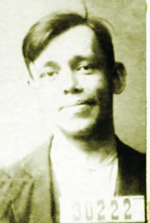Sepia arrest photograph of a young man in a jacket with his hair combed back, a numbered board reading 30222 held at his chest