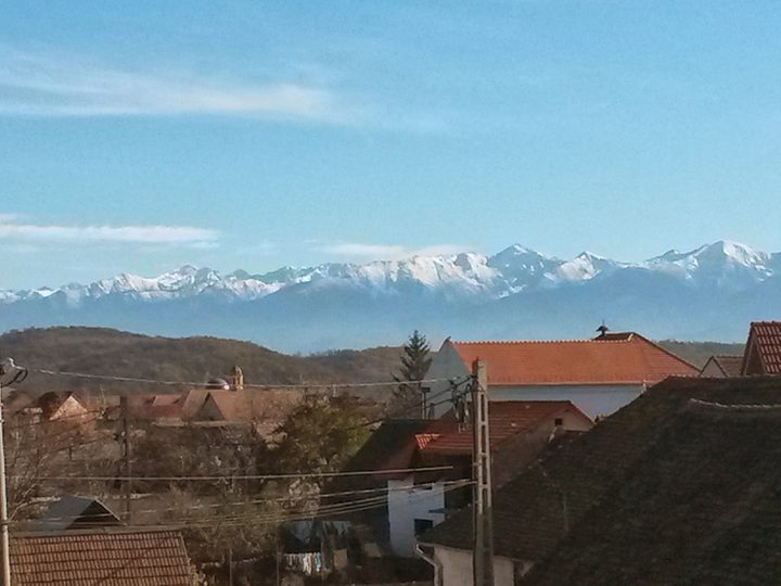 Tiled roofs and a church tower in the foreground with the snow covered Carpathian range filling the horizon behind, seen from Sibiu in November