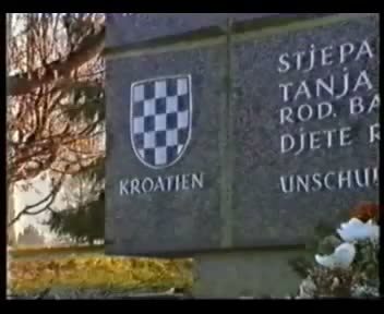 A television frame of a headstone in a cemetery carrying the family name and the three first names cut into the stone