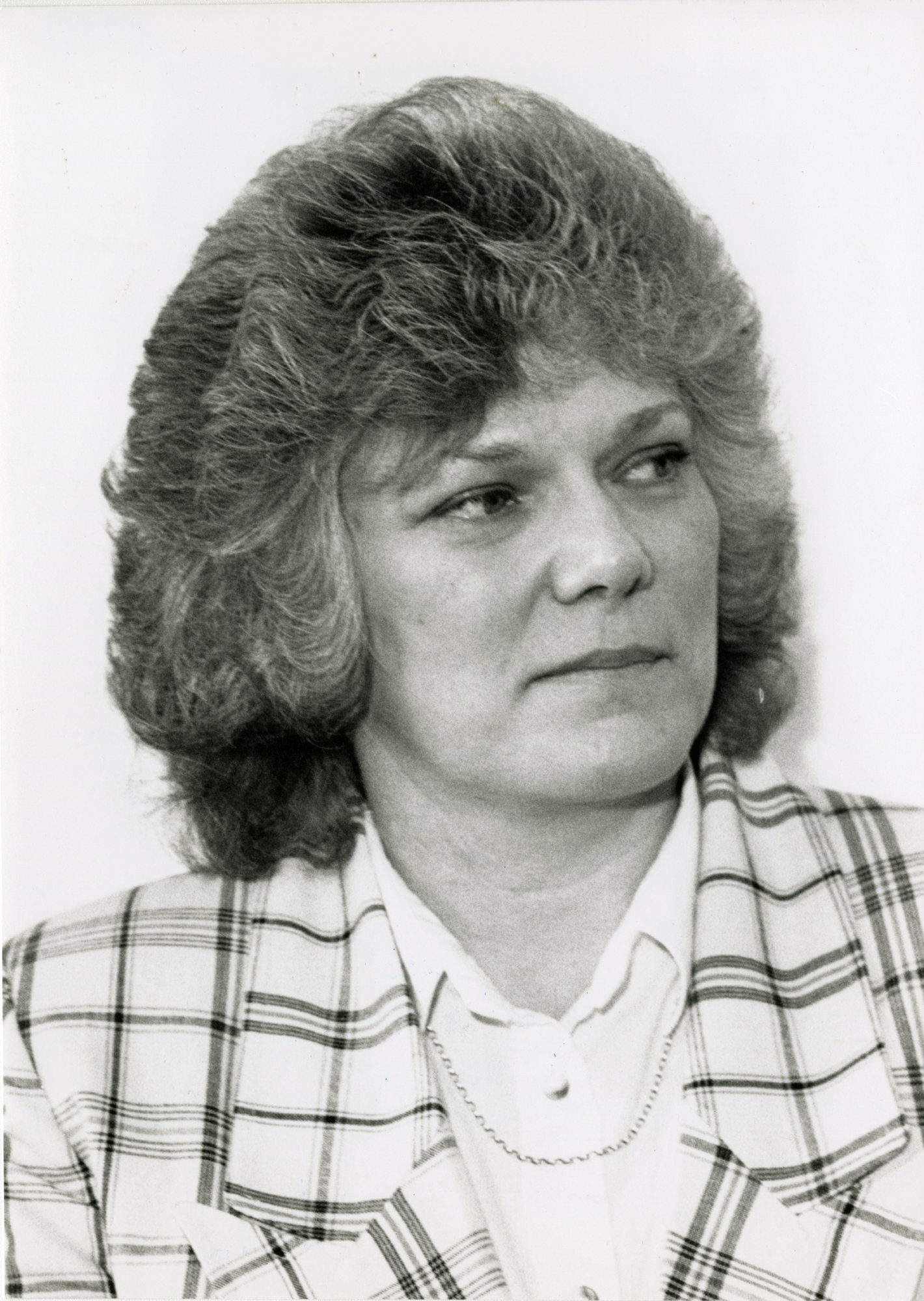 A black and white press portrait of Shirley Stedul, a woman in a checked jacket over a white blouse, looking away from the camera