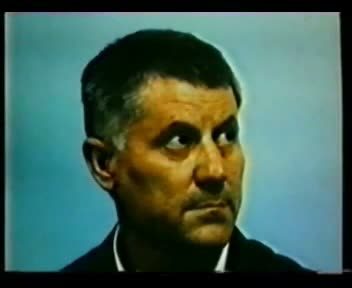 A television frame of a colour portrait photograph of Vinko Sindicic, a man with swept back grey hair in a dark jacket and white shirt, against a pale blue background