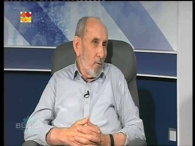 A television frame of an elderly Nikola Stedul with a white beard, in a light blue shirt, sitting in a studio armchair with his hands folded