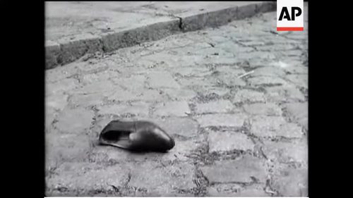 A staged newsreel frame of a man's shoe lying on cobbles, filmed as a reconstruction for a British newsreel in July 1952