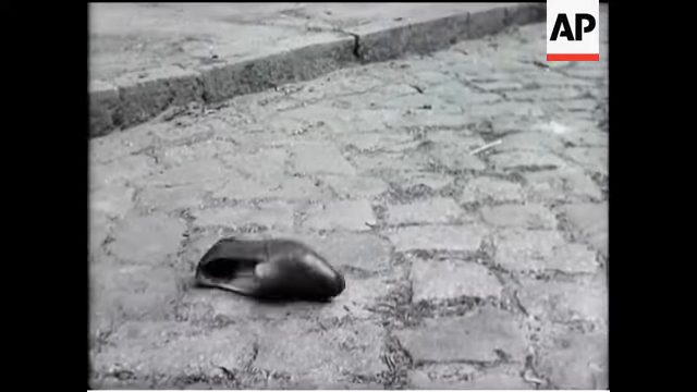 A staged newsreel frame of a man's shoe lying on cobbles, filmed as a reconstruction for a British newsreel in July 1952