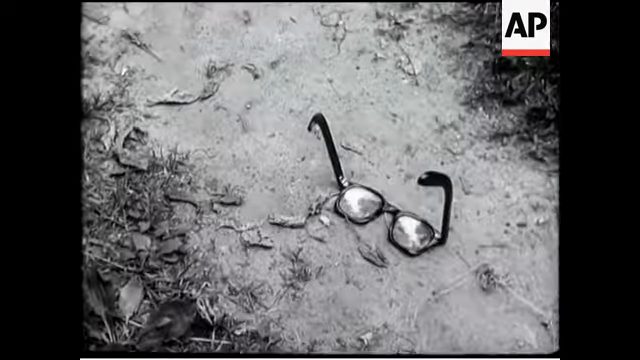 A staged newsreel frame of a pair of spectacles lying on the ground, filmed as a reconstruction for a British newsreel in July 1952