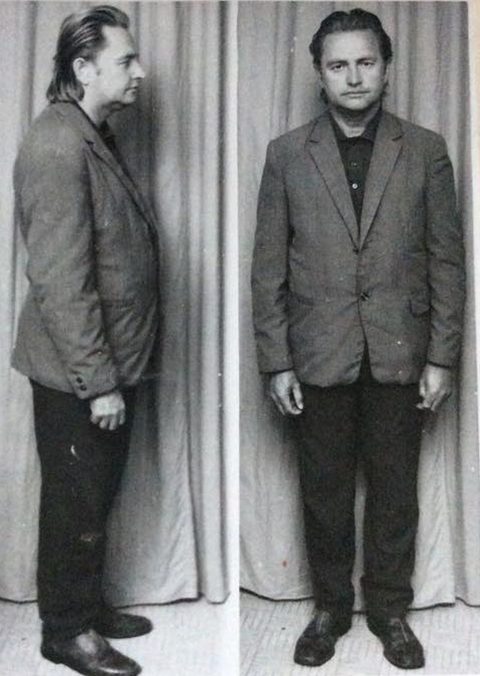 Two black and white full length militia identification photographs of the same man against a curtain, standing in profile on the left and facing the camera on the right, in a loose jacket and dark trousers