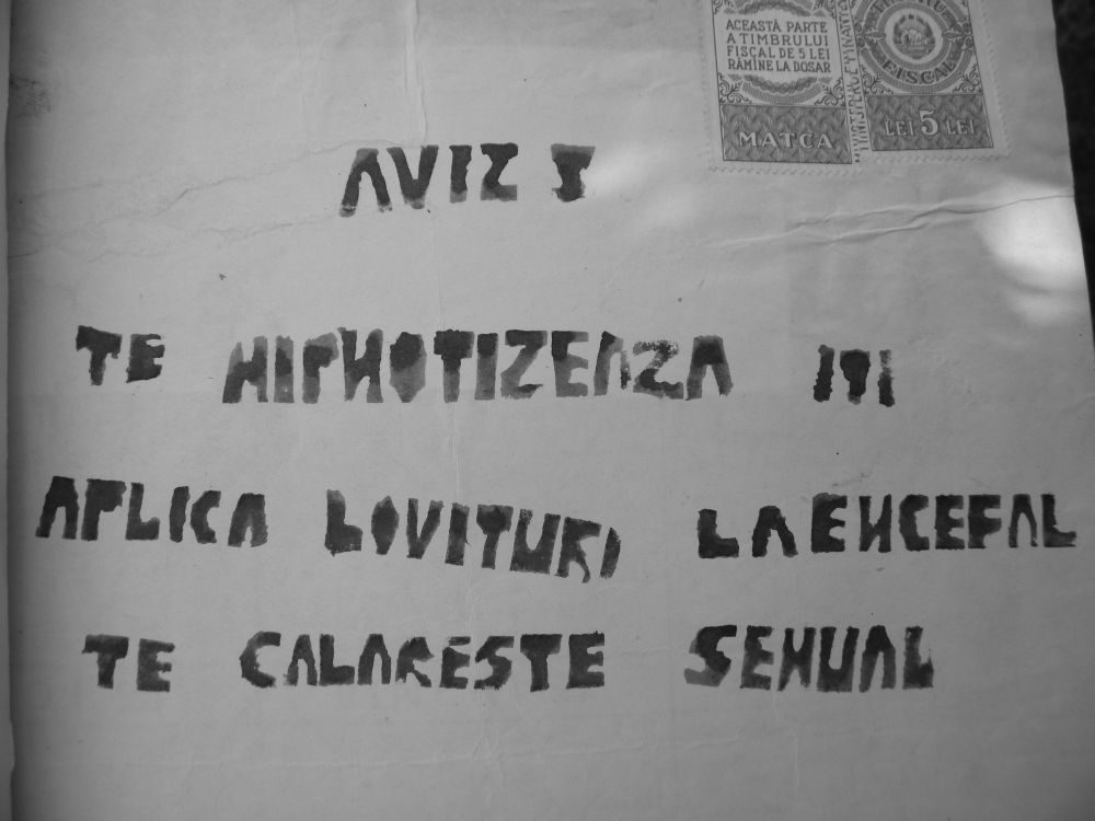 A sheet of paper photographed close up, hand stencilled in large block capitals in Romanian: AVIZ, TE HIPNOTIZEAZA, ITI APLICA LOVITURI LA ENCEFAL, TE CALARESTE SEXUAL, a warning that someone hypnotises you, strikes your brain and rides you sexually; a five lei fiscal stamp is fixed in the top corner