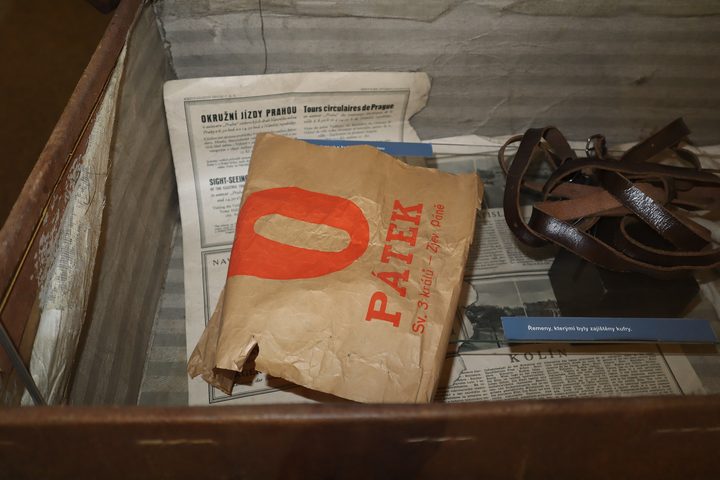 A torn printed wrapper lying on old newspapers inside the open suitcase, with the leather straps beside it