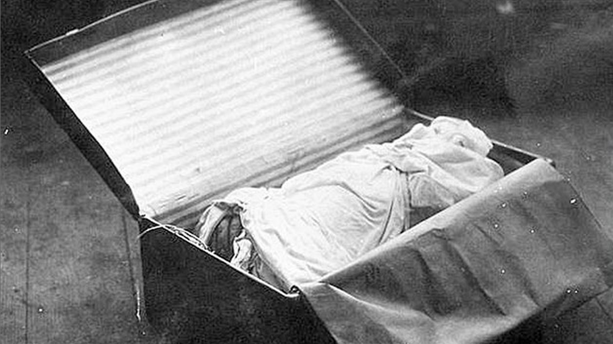The 1933 police photograph of one of the suitcases standing open on a floor, its lid back and its contents wrapped in sheets, with part of the remains showing at the near end