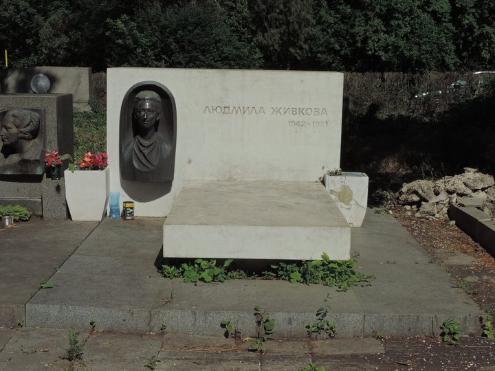 A low white stone memorial with a bronze bust of a young woman set into a niche, the stone cut with her name in Cyrillic and the years 1942 to 1981