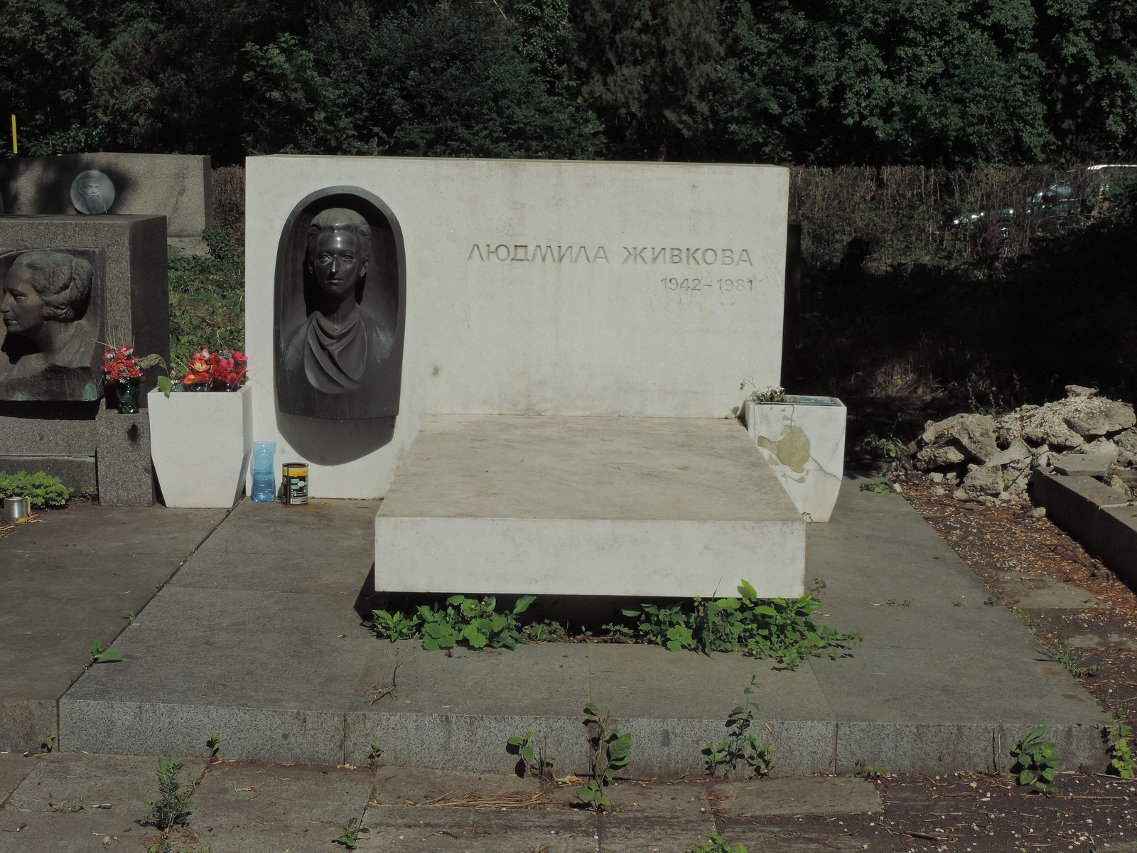 A low white stone memorial with a bronze bust of a young woman set into a niche, the stone cut with her name in Cyrillic and the years 1942 to 1981