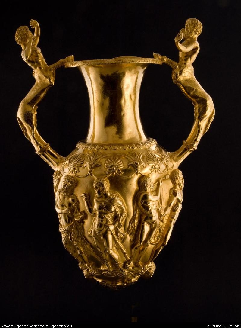 A gold vessel with two handles modelled as figures and a frieze of figures around its body, photographed against black