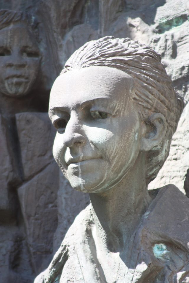 A close view of a cast relief on the monument: the head and shoulders of a woman with a band across her hair, a child's face carved behind her shoulder